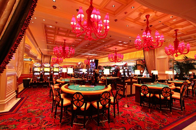 Ornate casino interior with red chandeliers, patterned red carpet, gaming tables and slot machines, warm luxurious mood